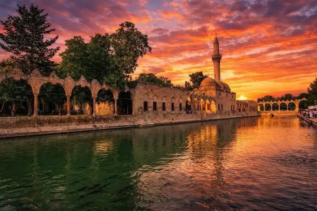 Sunset view of Balıklıgöl reflecting the historic Halil-ur Rahman Mosque and stone arches in Şanlıurfa, Turkey