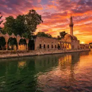 Sunset view of Balıklıgöl reflecting the historic Halil-ur Rahman Mosque and stone arches in Şanlıurfa, Turkey