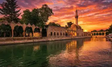 Sunset view of Balıklıgöl reflecting the historic Halil-ur Rahman Mosque and stone arches in Şanlıurfa, Turkey