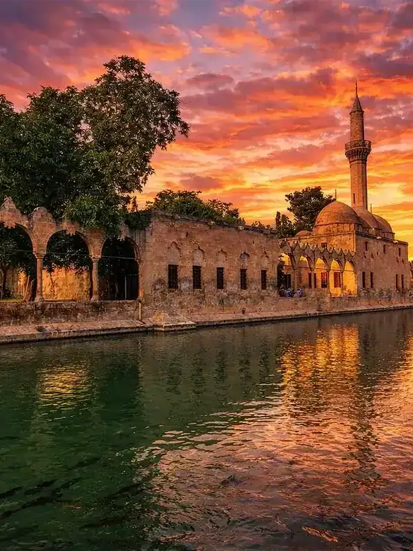 Sunset view of Balıklıgöl reflecting the historic Halil-ur Rahman Mosque and stone arches in Şanlıurfa, Turkey