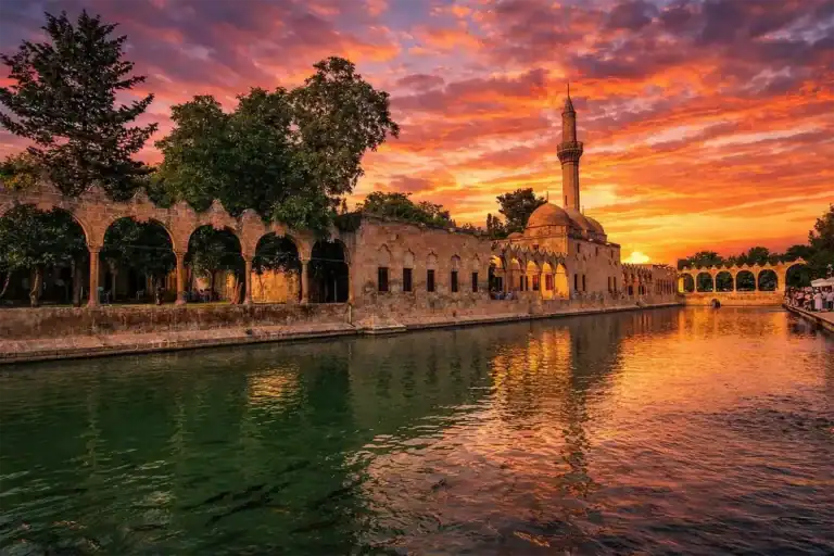 Sunset view of Balıklıgöl reflecting the historic Halil-ur Rahman Mosque and stone arches in Şanlıurfa, Turkey