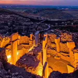 Ancient Göbekli Tepe archaeological site illuminated at dusk, showcasing its massive stone pillars a.