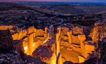 Ancient Göbekli Tepe archaeological site illuminated at dusk, showcasing its massive stone pillars a.