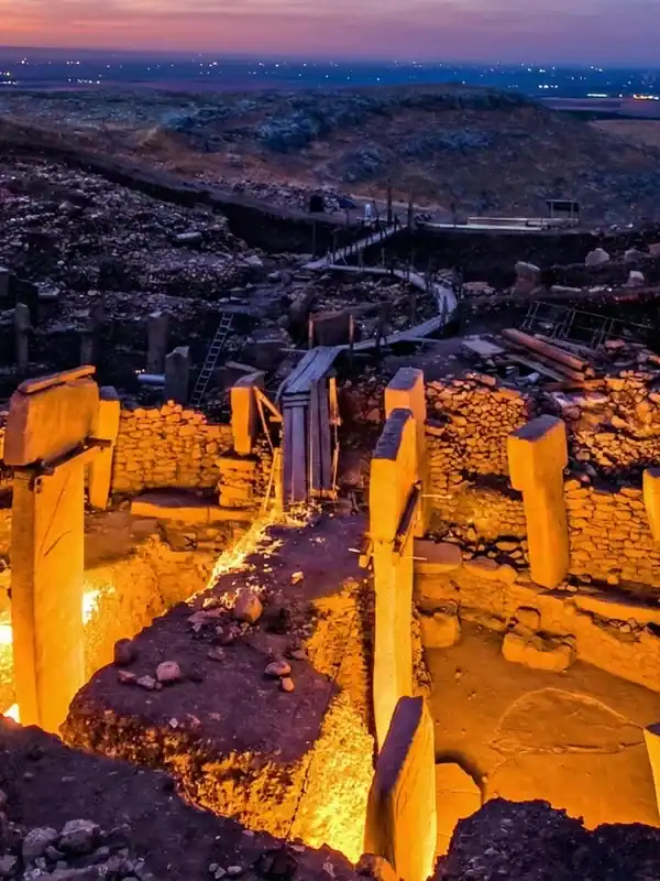 Ancient Göbekli Tepe archaeological site illuminated at dusk, showcasing its massive stone pillars a.