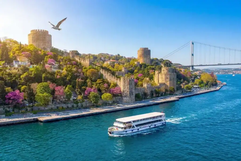 Scenic Bosphorus cruise boat sailing past the historical Rumeli Fortress and bridge in Istanbul on a sunny day.