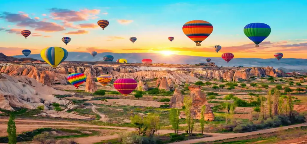 Dozens of brightly colored hot air balloons soaring over the rocky fairy chimneys and valleys of Cappadocia, Turkey, during a golden sunrise.