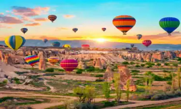 Dozens of brightly colored hot air balloons soaring over the rocky fairy chimneys and valleys of Cappadocia, Turkey, during a golden sunrise.