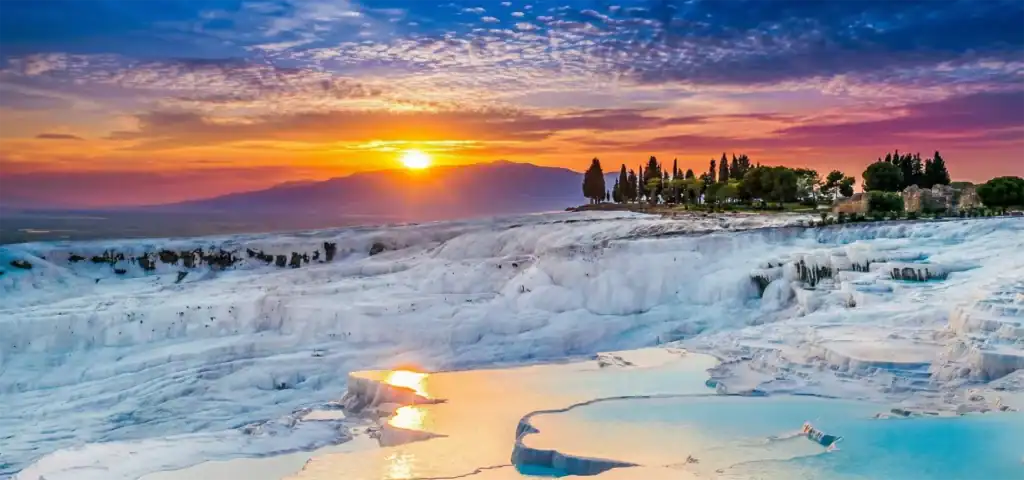 A vibrant sunset over the white travertine terraces and turquoise hot springs of Pamukkale, Turkey.