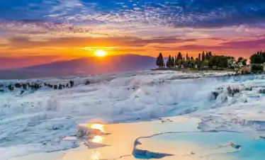 A vibrant sunset over the white travertine terraces and turquoise hot springs of Pamukkale, Turkey.