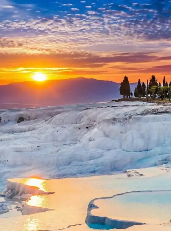 A vibrant sunset over the white travertine terraces and turquoise hot springs of Pamukkale, Turkey.