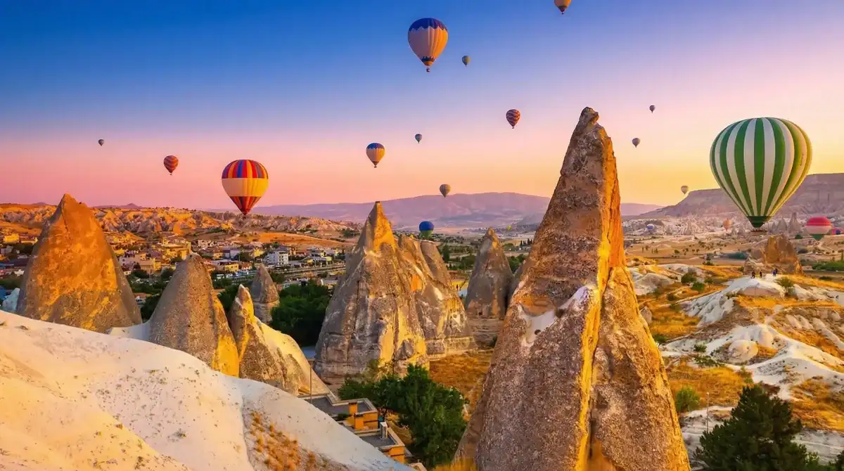 Dozens of vibrant hot air balloons floating gracefully over the illuminated, golden fairy chimneys of Cappadocia at sunrise, as One Nation Travel guides guests on a breathtaking aerial tour of the historic Turkish landscape.