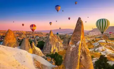 Dozens of vibrant hot air balloons floating gracefully over the illuminated, golden fairy chimneys of Cappadocia at sunrise, as One Nation Travel guides guests on a breathtaking aerial tour of the historic Turkish landscape.