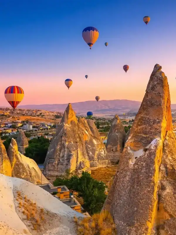 Dozens of vibrant hot air balloons floating gracefully over the illuminated, golden fairy chimneys of Cappadocia at sunrise, as One Nation Travel guides guests on a breathtaking aerial tour of the historic Turkish landscape.
