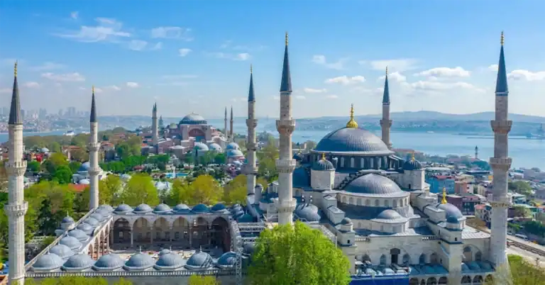 Hagia Sophia vs. Blue Mosque: Key Differences Explained 1 Aerial view of Istanbul: The six-minaret Blue Mosque and the Hagia Sophia stand prominently. Sultanahmet Park is between them, with the Bosphorus Strait and distant city skyline under a clear sky.