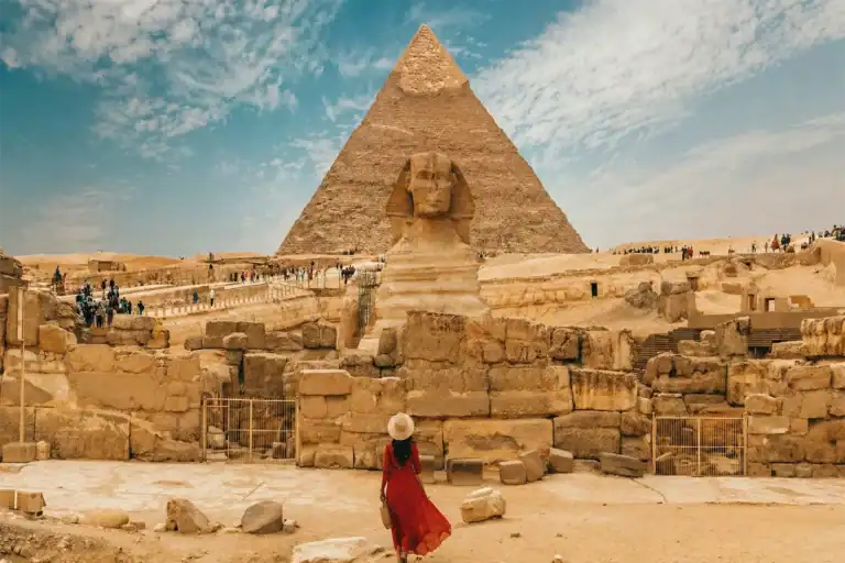 Woman walking toward the Great Sphinx and Pyramid of Giza under a partly cloudy sky in Egypt