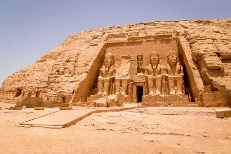 Abu Simbel temple façade with colossal Ramses II statues carved into sandstone cliff under clear desert sky in Egypt