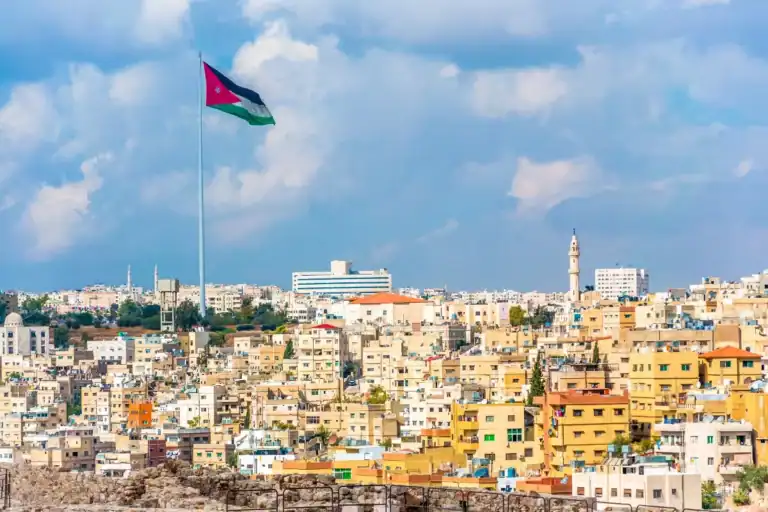 Amman city skyline with giant Jordan flag, beige buildings, and mosque towers under dramatic cloudy skies