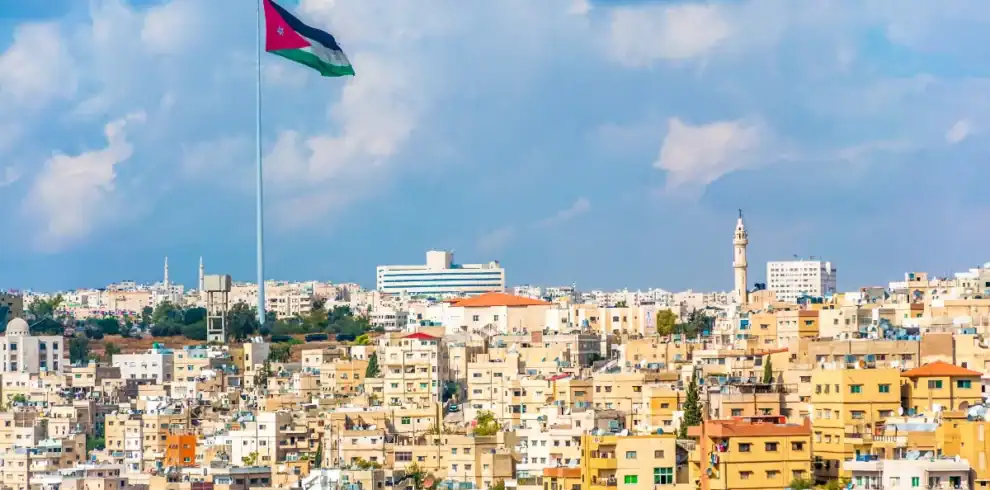 Amman city skyline with giant Jordan flag, beige buildings, and mosque towers under dramatic cloudy skies