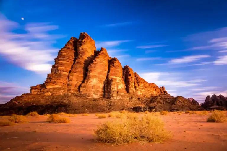 Towering red sandstone cliffs and dry shrubs glow beneath a deep blue sky in the Wadi Rum desert, Jordan