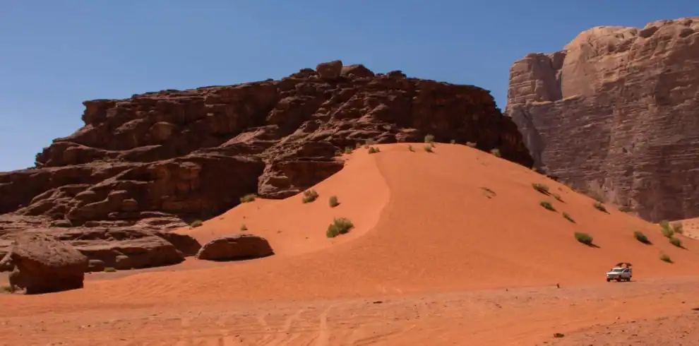 Wadi Rum desert sands with towering red rock formations and jeep safari adventure under a clear blue sky