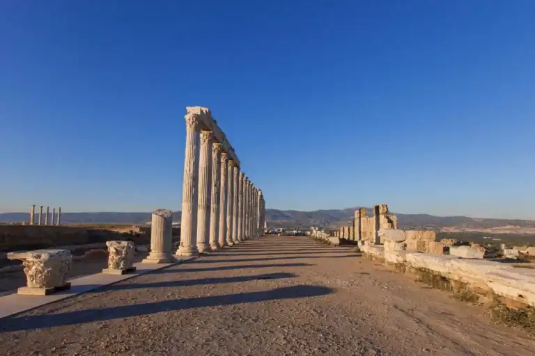 Laodicea colonnaded street in Denizli, Turkey, with ancient stone ruins and mountain views under blue sky