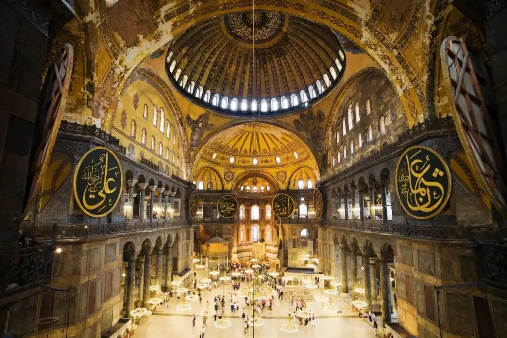 Hagia Sophia interior in Istanbul, Turkey, showing golden dome, Arabic calligraphy, chandeliers, and visitors