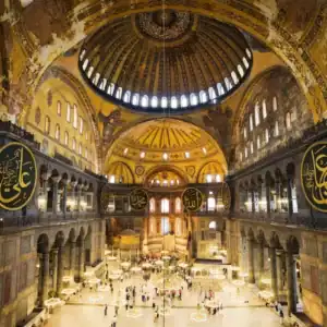 Hagia Sophia interior in Istanbul, Turkey, showing golden dome, Arabic calligraphy, chandeliers, and visitors