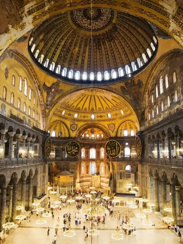 Hagia Sophia interior in Istanbul, Turkey, showing golden dome, Arabic calligraphy, chandeliers, and visitors