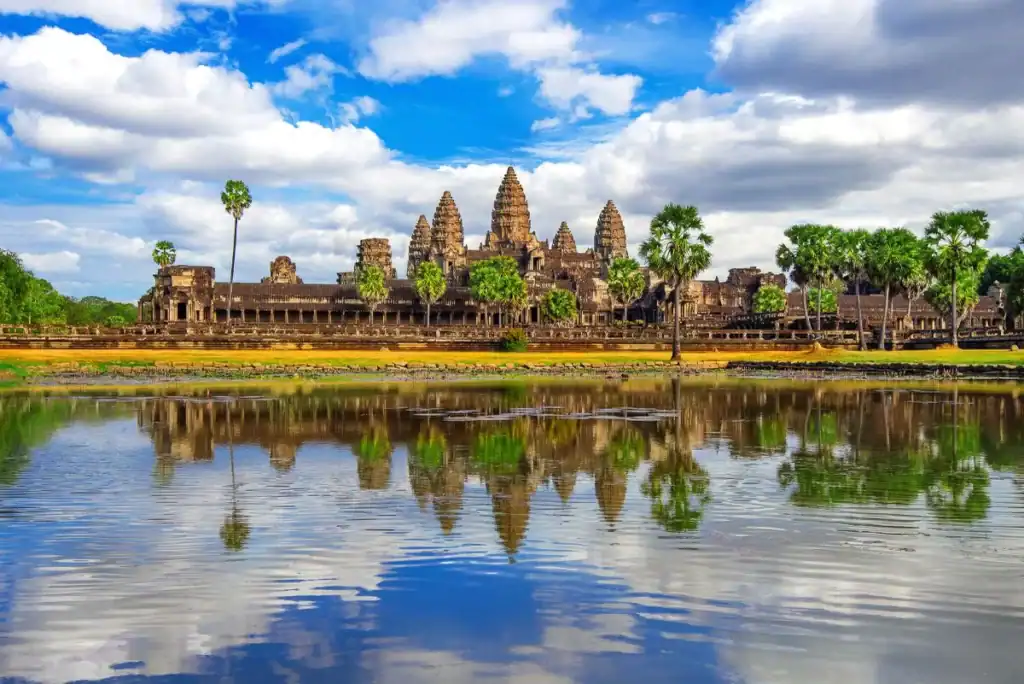 Angkor Wat temple in Siem Reap, Cambodia, reflected in a peaceful pond under a blue sky.