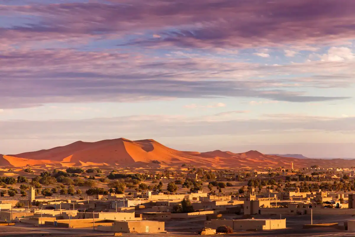 Panoramic view of Merzouga and the Erg Chebbi sand dunes glowing at sunset in Morocco.