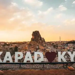Cappadocia sunset view with Ortahisar rock castle, hillside homes, mosque minaret, and Kapadokya heart sign.