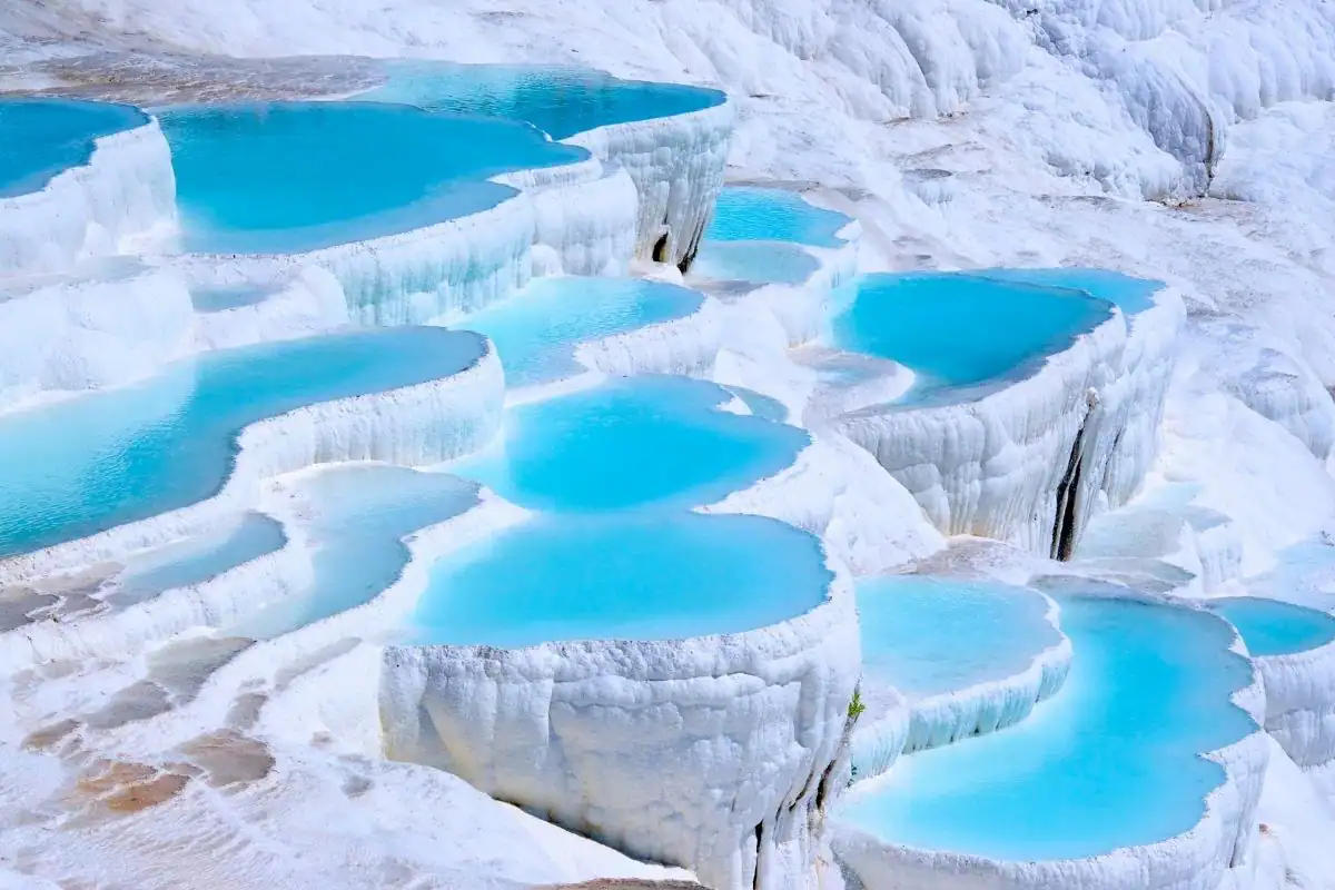 Pamukkale mineral-rich thermal water fills turquoise pools cascading over bright white travertine terraces in Türkiye.