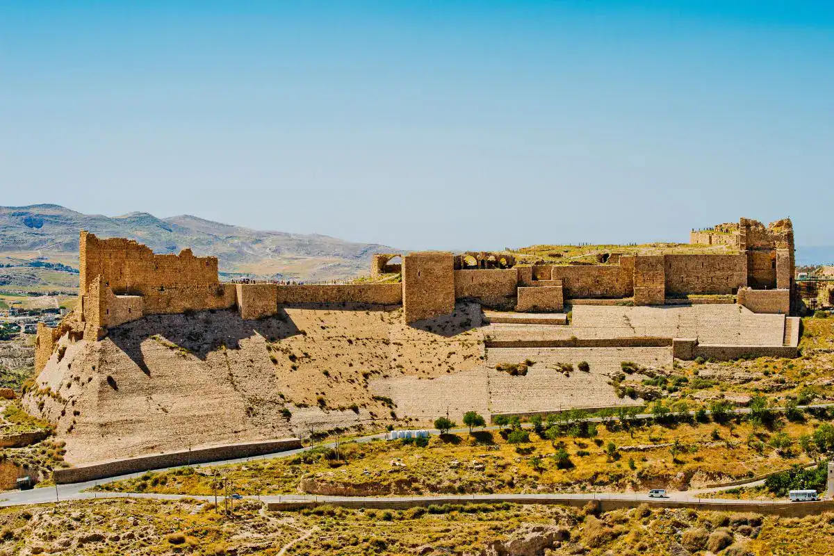 Historic stone fortress with massive defensive walls overlooking a dry, mountainous landscape under a clear blue sky.