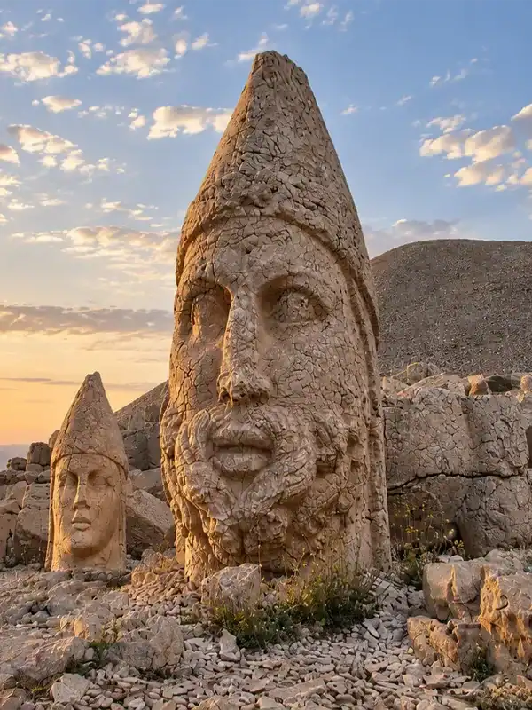 Mount Nemrut stone heads and ancient statues illuminated by a golden sunrise over the rugged summit landscape.