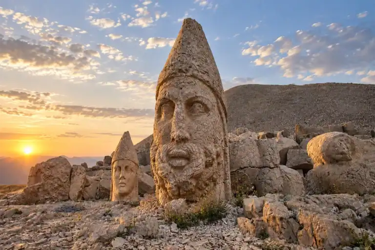 Mount Nemrut stone heads and ancient statues illuminated by a golden sunrise over the rugged summit landscape.