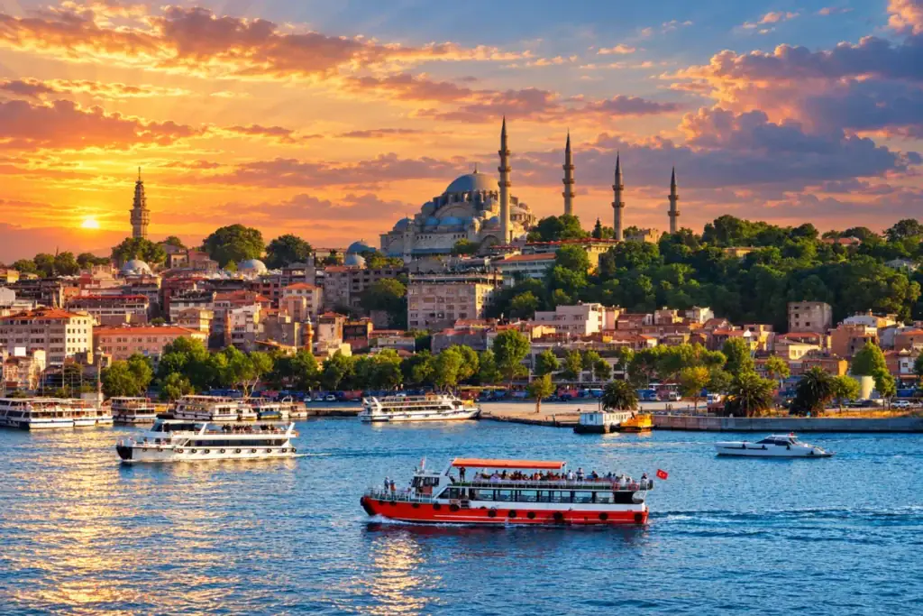 Istanbul skyline at sunset with Süleymaniye Mosque, colorful waterfront buildings, and ferries crossing the Golden Horn.